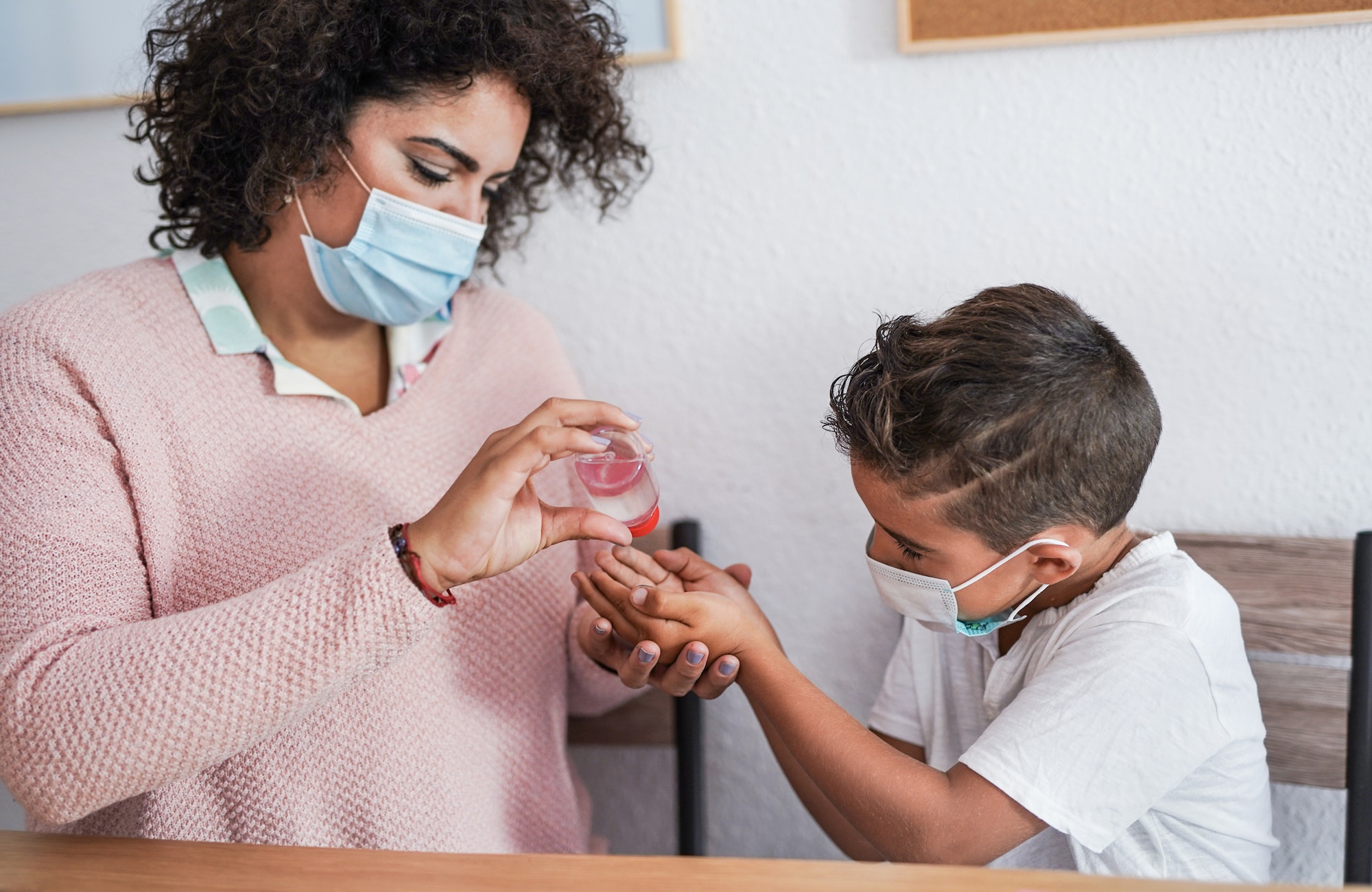 Teacher disinfect hand of child while wearing surgical face mask for coronavirus outbreak
